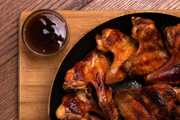Baked chicken wings with sauce cooked in a pan on a wooden background. Side view. Fast food.
