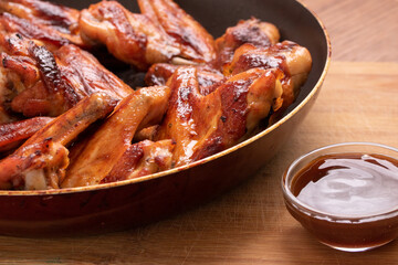 Baked chicken wings with sauce cooked in a pan on a wooden background. Side view. Fast food.