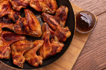 Fried spicy chicken wings with sauce on a pan on a wooden background. The view from the top. Fast...