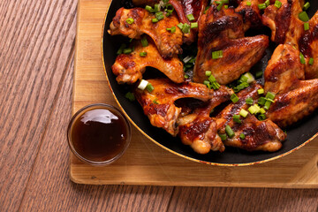 Fried spicy chicken wings with sauce on a pan on a wooden background. The view from the top. Fast food.