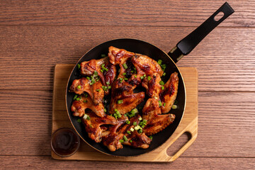 Fried spicy chicken wings with sauce on a pan on a wooden background. The view from the top. Fast food.