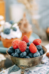 Blueberries raspberries in a Cup on a wooden table. Berry mix for desserts, with a blurry background.