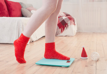 Female feet standing on electronic scales for weight control in red socks with Christmas decoration