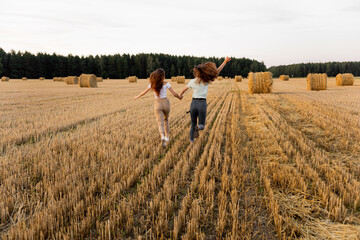Two young girls run a race across the field near autumn forest. Two girls run across the field to...