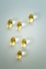 Fototapeta na wymiar Six shiny yellow Vitamin D, fish oil capsule on white