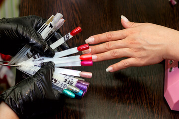 Fototapeta premium girl chooses color of nail polish for manicure in beauty salon using plastic samples