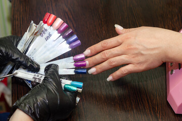 girl chooses color of nail polish for manicure in beauty salon using plastic samples