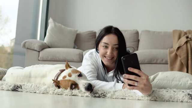 Young woman takes a selfie with her dog and use phone in a beautiful modern apartment