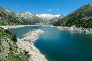 Fototapeta na wymiar Dam in Austrian Alps. The artificial lake stretches over a vast territory, shining with navy blue color. The dam is surrounded by high mountains. In the back there is a glacier. Controlling the nature