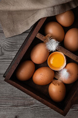 Chicken eggs in a wooden box with two feathers on a wooden background