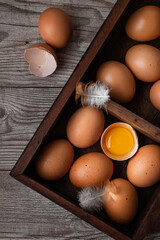Chicken eggs in a wooden box with two feathers on a wooden background