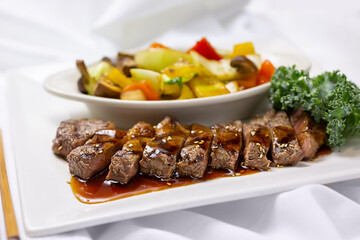 A view of a plate of beef teriyaki, in a restaurant or kitchen setting.