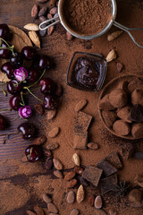 art background with healthy delicious dark truffles, chocolate  and  ingridients:  natural cocoa beans,  powder, chocolate,  ripe cherry. healthy sweets concept. flat lay
