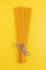 Uncooked spaghetti tied with twine on yellow background. Vertical photo.