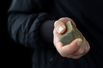 Cobblestone in male hand on black background. Riot concept.