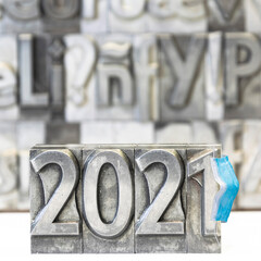 Happy new year 2021 on background with press types from which a blue surgical mask hangs