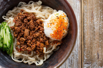 A top down view of a Taiwanese noodle bowl featuring diced pork, tofu, poached egg and cucumbers.