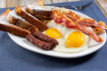 A view of a French toast breakfast plate, featuring sunny side up eggs and bacon strips.