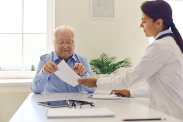 Obraz premium Smiling woman doctor giving paper prescription to elderly man patient in clinic
