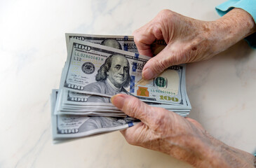 Close-up of an elderly woman's hands holding money in 100 dollar bills