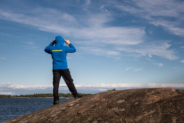 Man standing on the cliff by the water wearing proudly a hoodie with Sweden text - 395977853