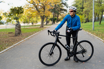 Obraz premium An athlete in glasses and a protective bicycle helmet stands in the park on a bicycle road. Sports and outdoor recreation.