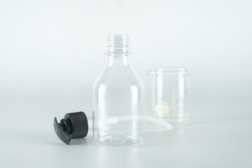 Uncover one empty transparent container spray plastic bottle for liquid gel, alcohol gel, lotion, cream, shampoo, isolated with an empty beaker on gray background.