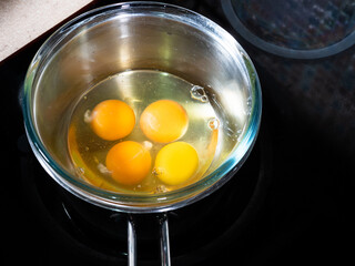 cooking sweet sponge cake at home - above view of four eggs in glass bowl on water bath on stove at home kitchen