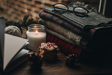 Scandinavian hygge styled Christmas composition. Cozy winter homely scene with candle and sweaters. Christmas cookies in a stack tied with thread.