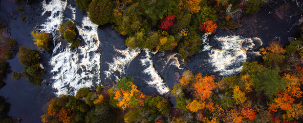 Incredible panoramic travel aerial look down photograph of Bond Falls Scenic Site including the upper and lower waterfalls and rapids in autumn with fall colored foliage on the treetops below.