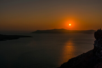 The sun sinks low in the sky viewed from Thira, Santorini at sunset in summertime