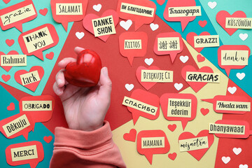 Thank You in many languages. Paper art, creative flat lay, top view on paper tags. International Thank you day. Creative background on colored paper. Hand with stone heart.