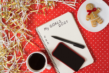 Phrase My Goals 2021 in a notebook, black pen and smart phone. Gingerbread and coffee on red...