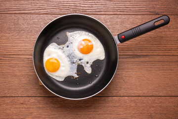 fried eggs from two eggs in a frying pan on a wooden background, top view, flat lay food