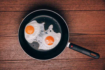 fried eggs from two eggs in a frying pan on a wooden background, top view, flat lay food