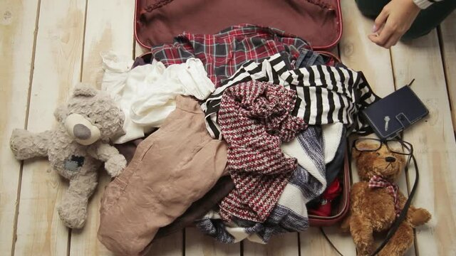 Faceless traveler woman trying to pack clothes in full owerflowing overfilled luggage. Mess nad disorder concept. Preparing for travel. Girl packing crammed suitcase. Tourism, journey lifestyle.