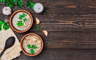 Fototapeta na wymiar Khash in a bowl. Traditional Armenian soup dish, meat broth, served with vegetables, garlic and national bread lavash. Clay plates, wooden background with copy space