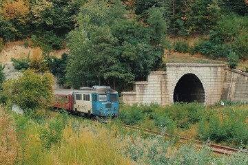 Fototapeta premium Train speeding at the exit of a tunnel in an remote mountain area