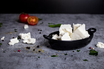 Feta traditional Greek cheese in a black tray with tomato on grey background