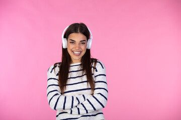 Image of a happy young beautiful woman posing isolated over pink wall background listening music with earphones. Romantic woman in warm jumper looking away with  earphones