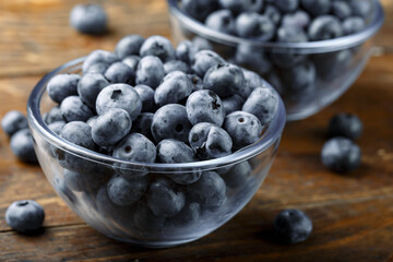 Fresh blueberries in a glass bowl and scattered on a wooden table. Foods containing antioxidants.