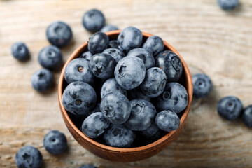 Fresh blueberries in a clay bowl and scattered on a wooden table. Foods containing antioxidants.
