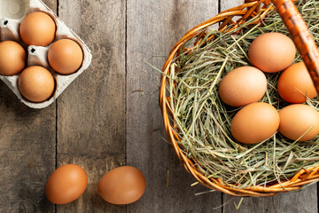 Chicken eggs in a hay basket and egg tray, on a wooden table.