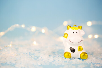 Obraz na płótnie Canvas Ceramic toy white cow with gold spots-a symbol of the new year 2021. Christmas blue background with garland lights in blur, copy space