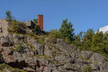 Fototapeta na wymiar Red brick chimney sticking from rock on Vallisaari island located between Helsinki and Suomenlinna. Despite small size there are fortifications, buildings, and a record-breaking range of species.