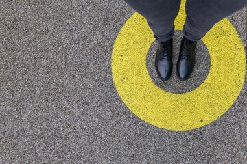 Black shoes standing in yellow circle on the asphalt concrete floor. Comfort zone or frame concept. Feet standing inside comfort zone circle. Place for text, banner - obrazy, fototapety, plakaty