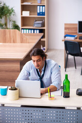 Young male employee drinking alcohol at workplace