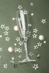 one glass lies on a green background and sparkling confetti stars. Festive concept top view.