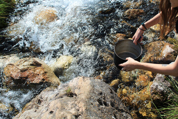 Camping life. Woman draws water from a mountain river into a cooking pot