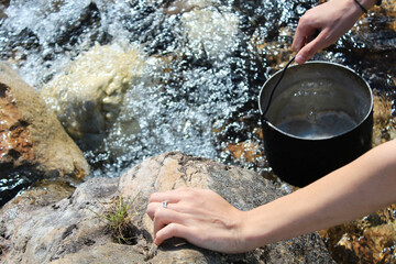 Camping life. Woman draws water from a mountain river into a cooking pot